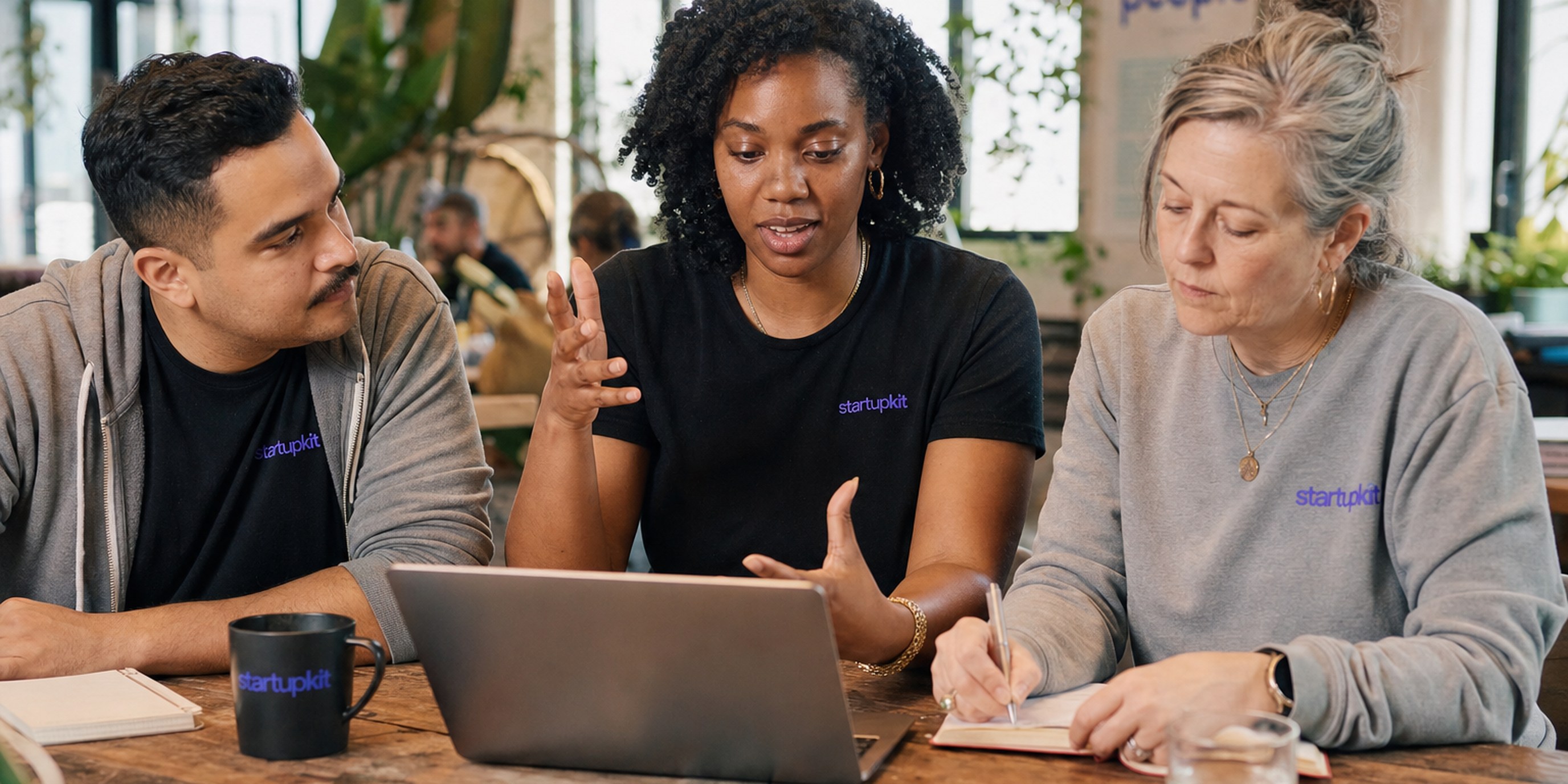 A startup hiring manager reading a candidate summary on her laptop in a sunlit co-working loft, making the final call herself instead of letting a model decide