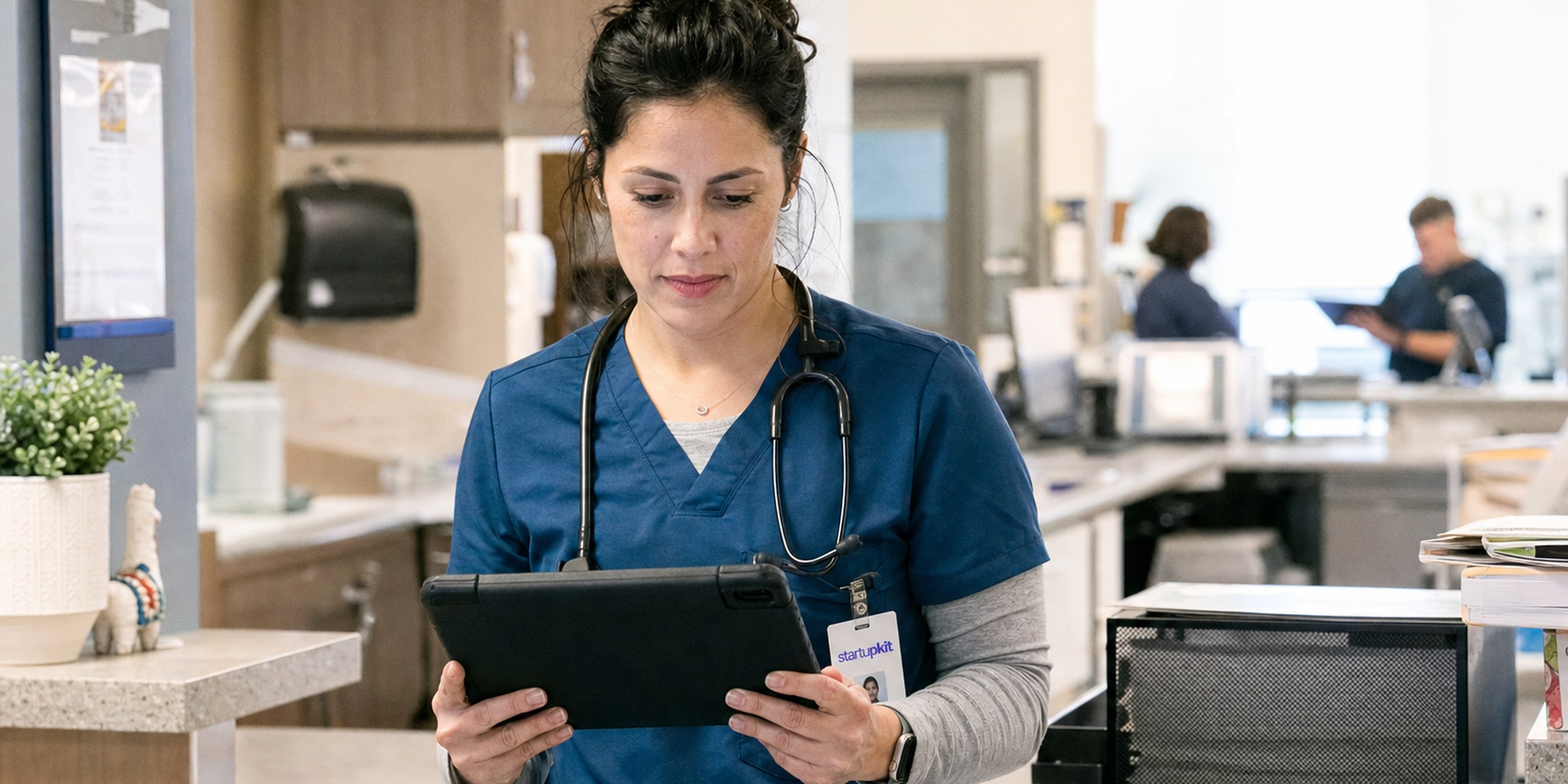 Certified physician assistant in scrubs reviewing a patient chart on a tablet at a clinic workstation during hiring onboarding