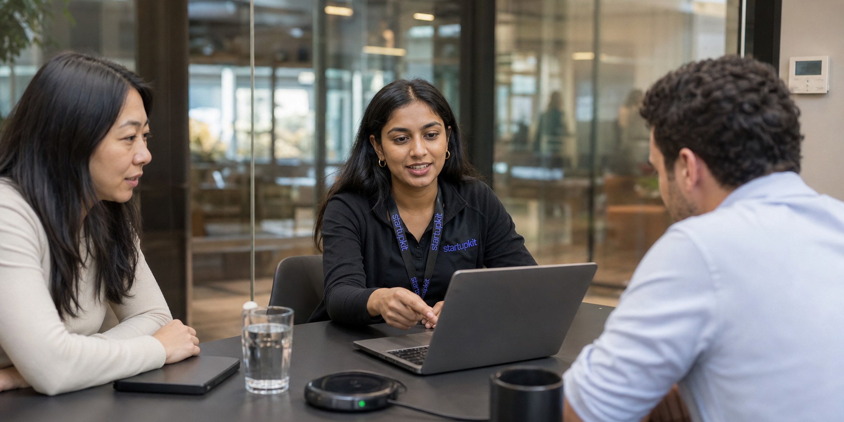 A solutions engineer running a tailored product demo on a laptop for two prospect stakeholders in a glass conference room
