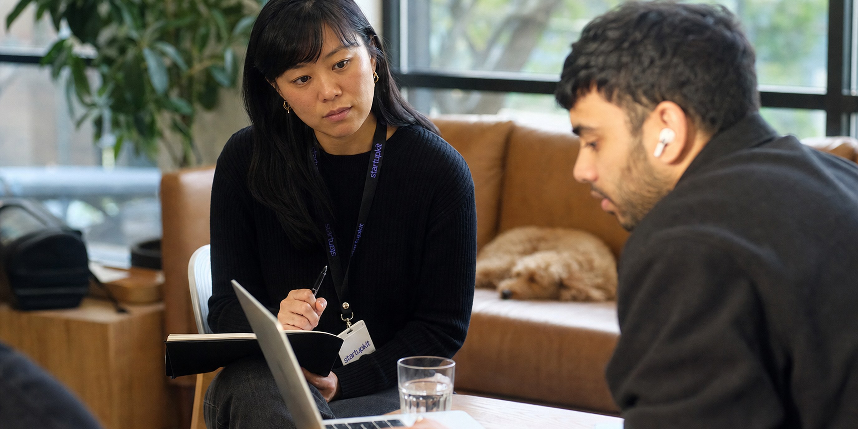 A UX researcher taking notes while observing a participant complete a usability test on a laptop in a moderated session